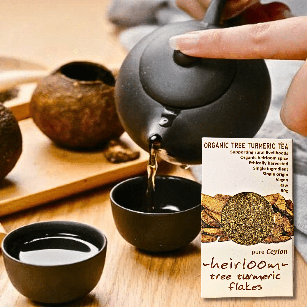 Hand pouring hot tea into small cups with a box of Organic Tree Turmeric Tea (heirloom tree turmeric flakes, 50 g, pure Ceylon) displayed beside the teapot.